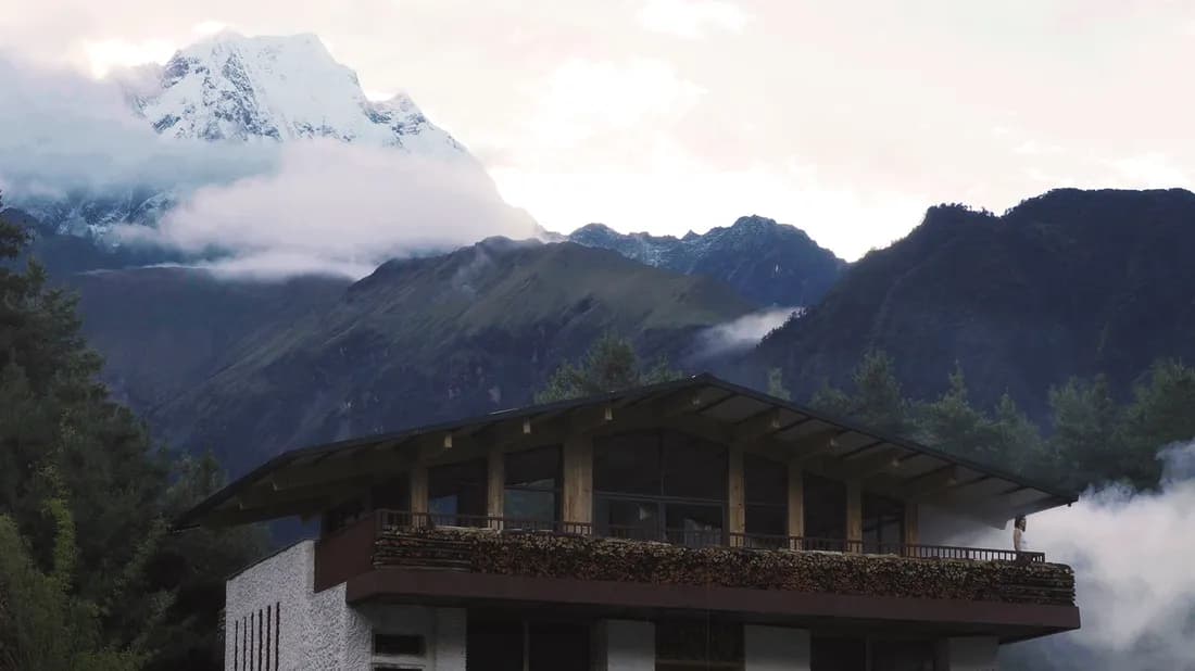 Timber lodge with a firewood-stacked balcony below snow-capped Himalayan peaks