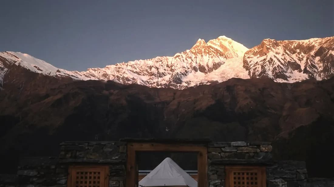 Canvas tent peak behind the stone gateway with the Annapurna range lit at sunrise