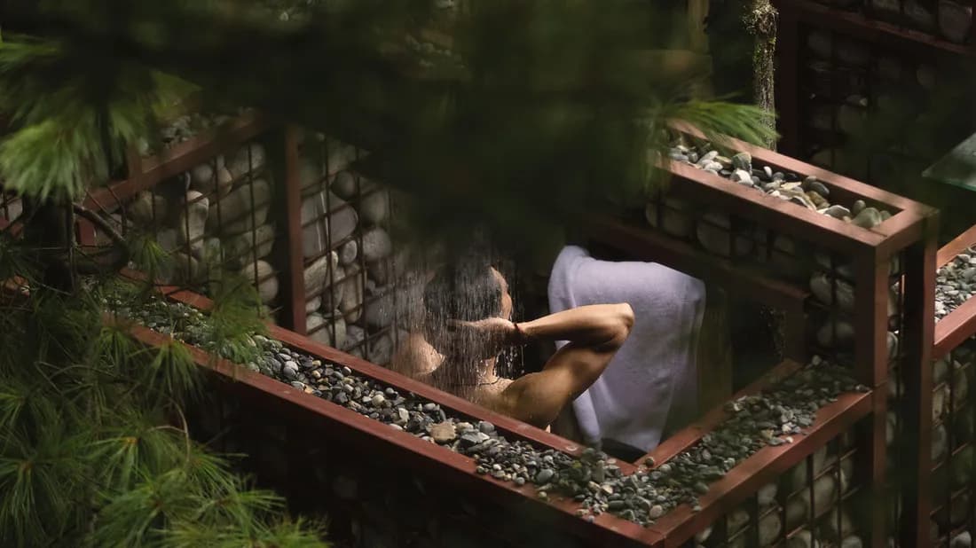 Open-air stone shower among pine branches at the camp