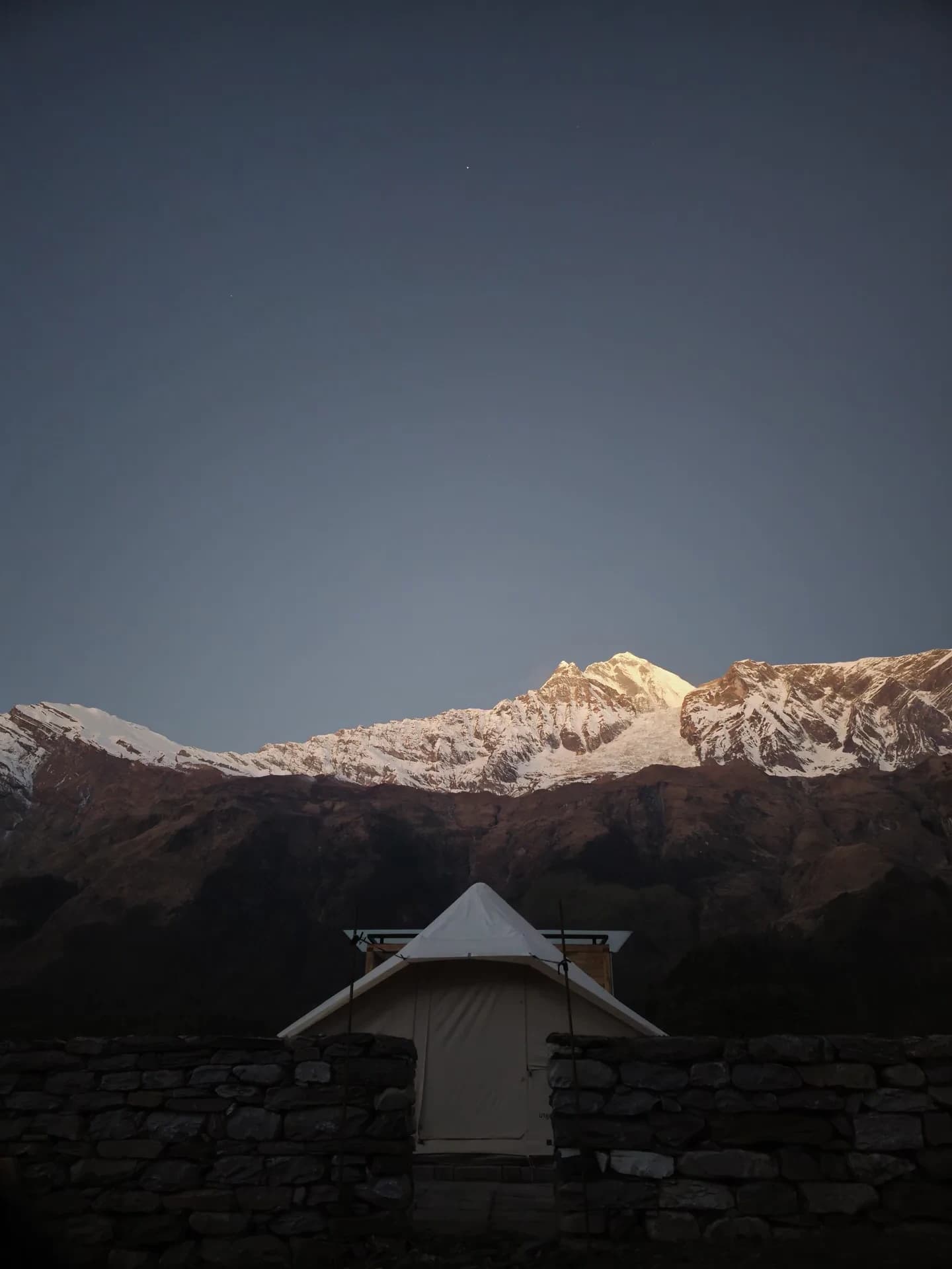 Canvas tent behind a stone wall below the sunlit Annapurna ridgeline