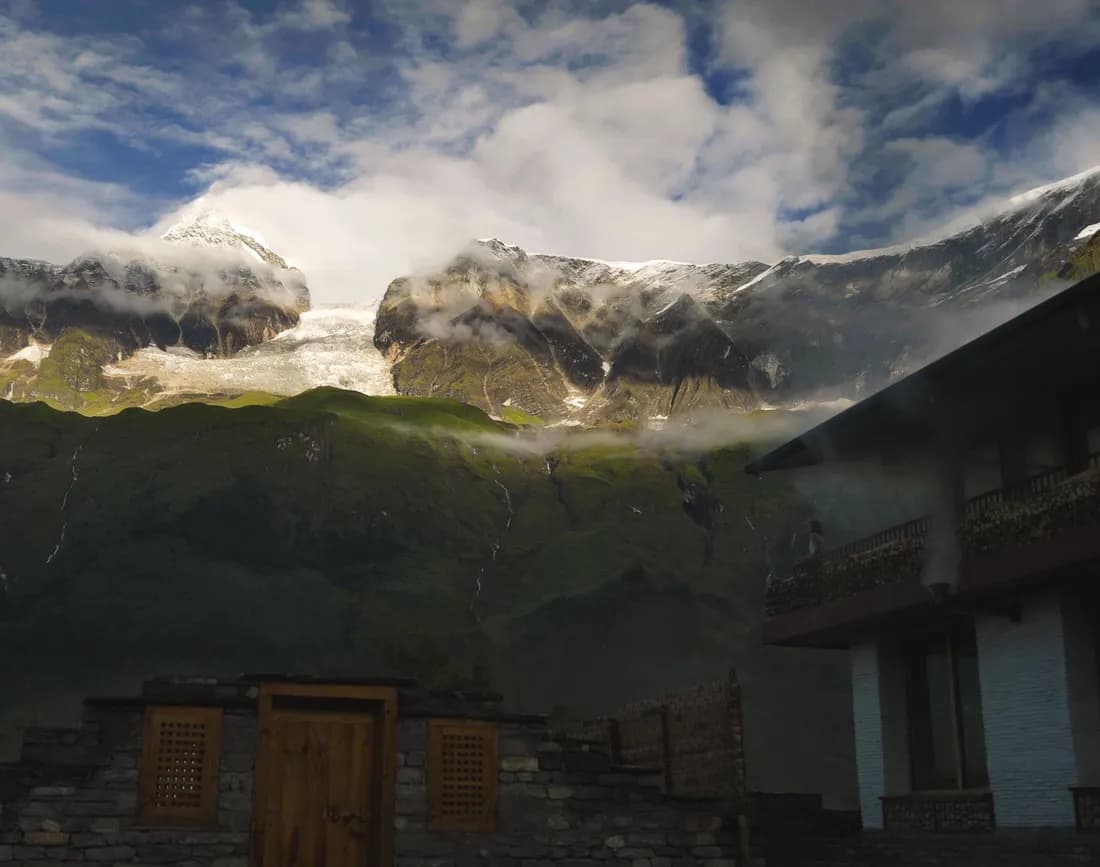 Stone gateway and lodge below cloud-draped snow peaks at the camp
