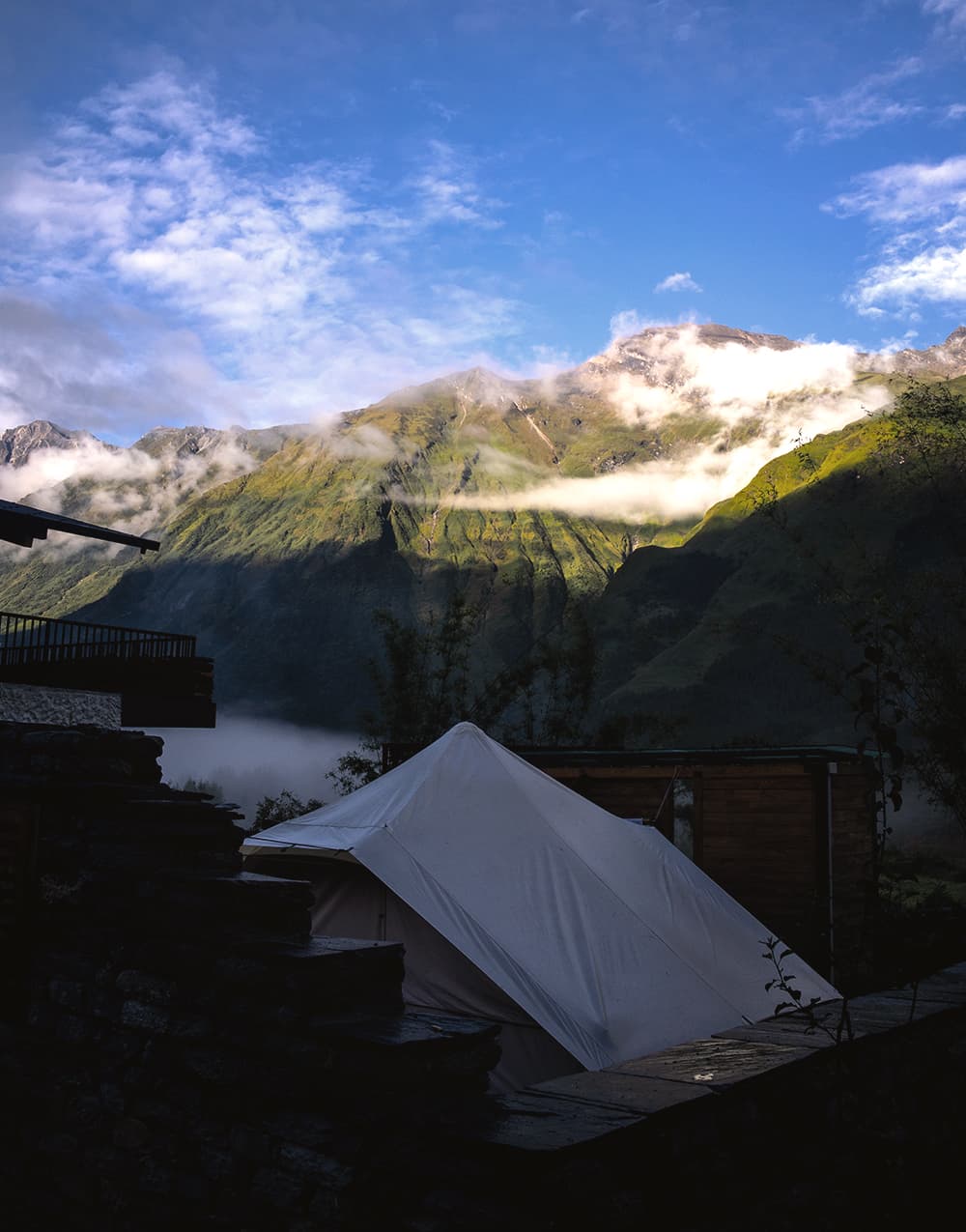 Canvas tent on a stone terrace at sunrise with the green valley beyond
