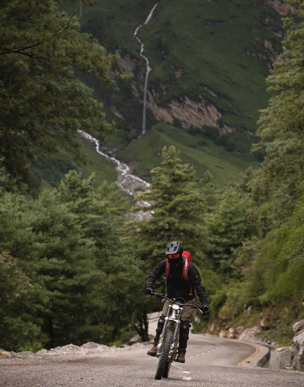 E-bike rider on a forest road with a waterfall on the hillside behind