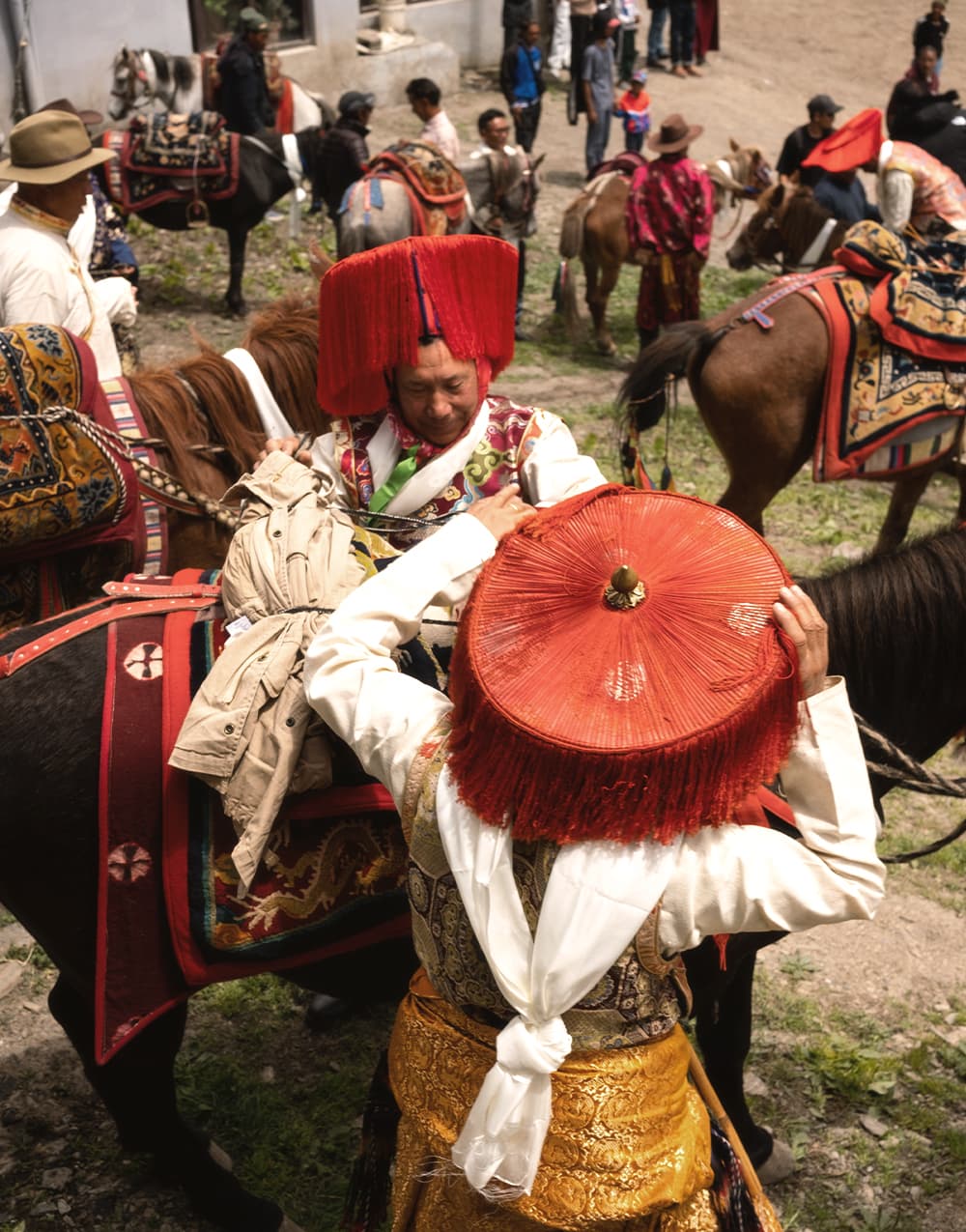 Festival horsemen in red-fringed hats and brocade preparing to ride