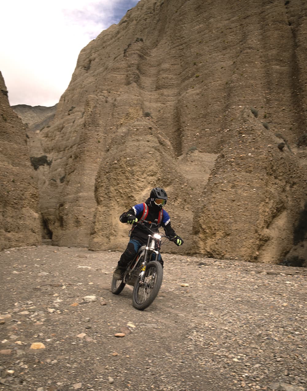 E-bike rider crossing a gravel wash beneath towering canyon walls
