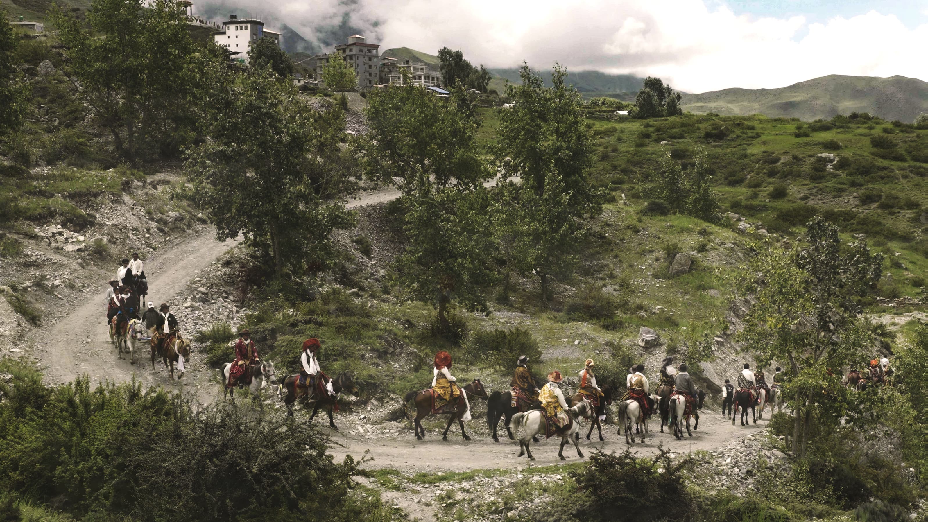 Procession of riders in traditional dress winding up a village trail