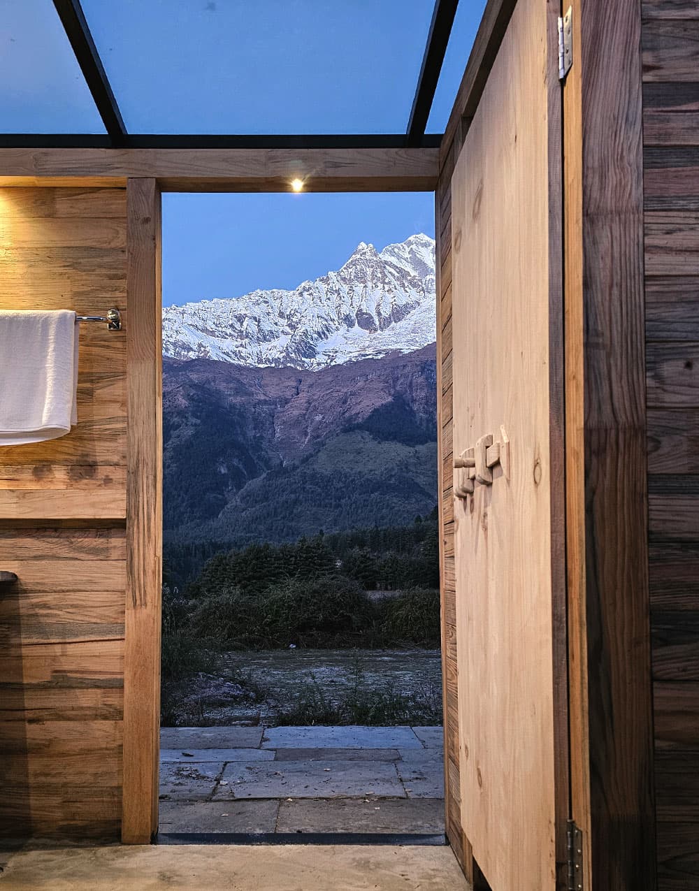 Snow peak framed through the open door of a timber cabin at dusk