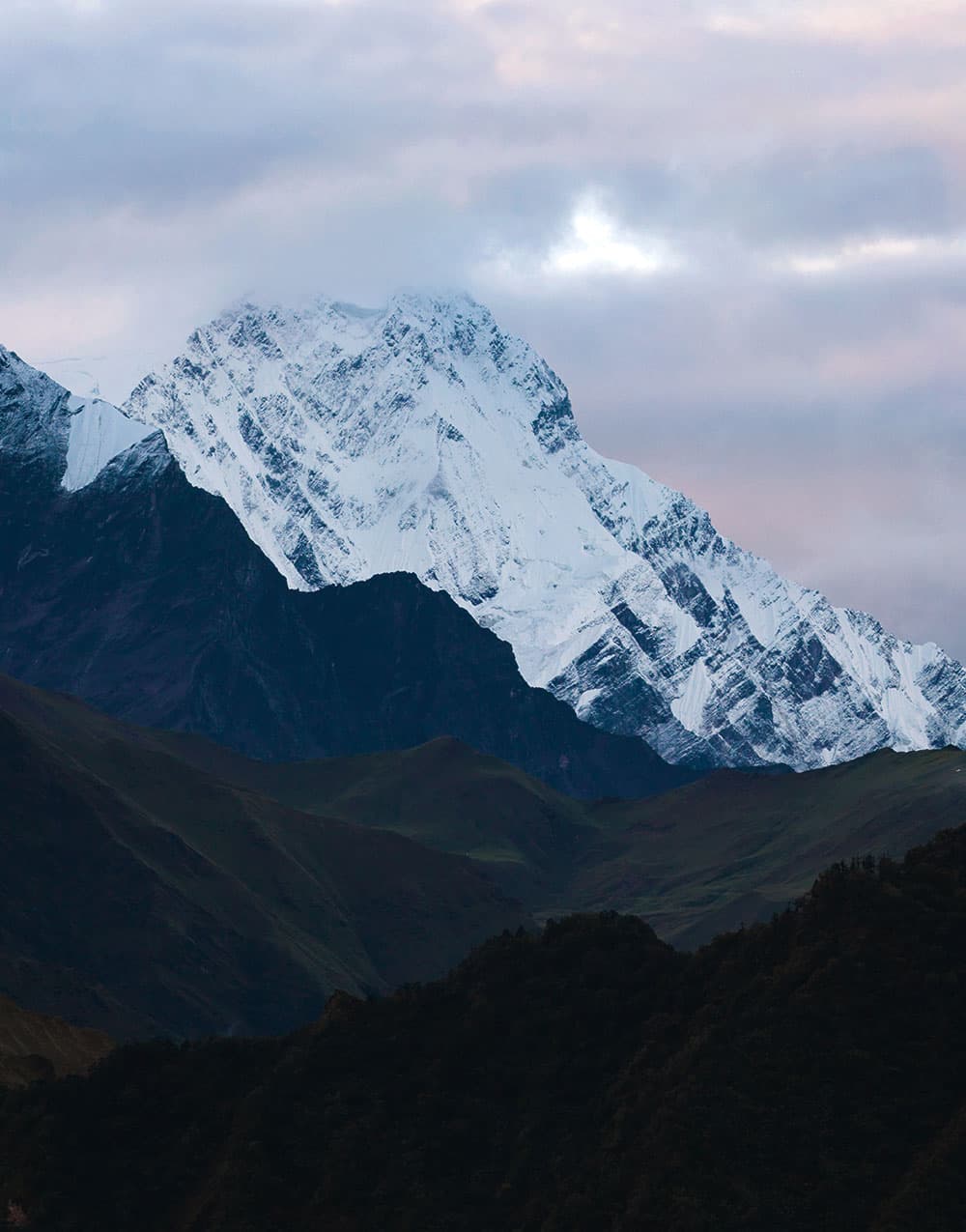 Snow peak glowing at dusk above dark green foothills
